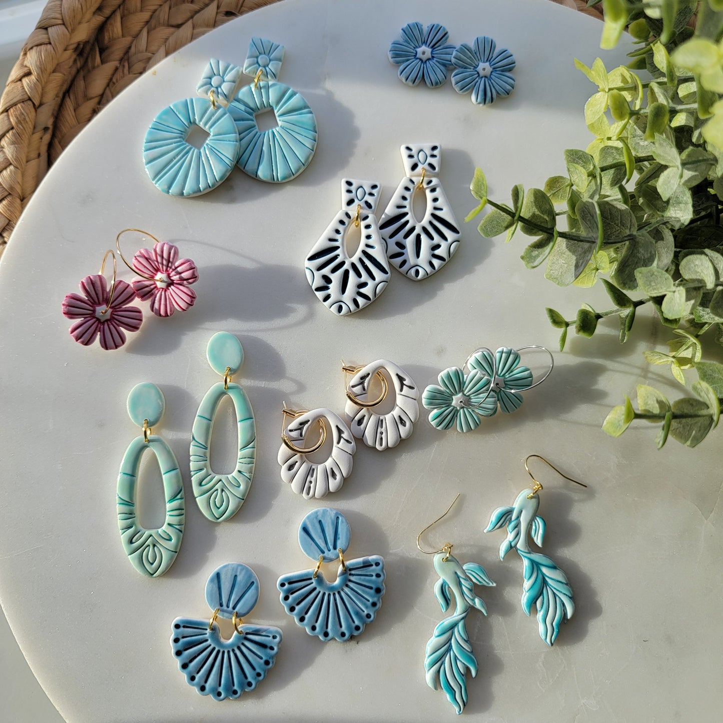Assorted earrings on a white surface with greenery in the background