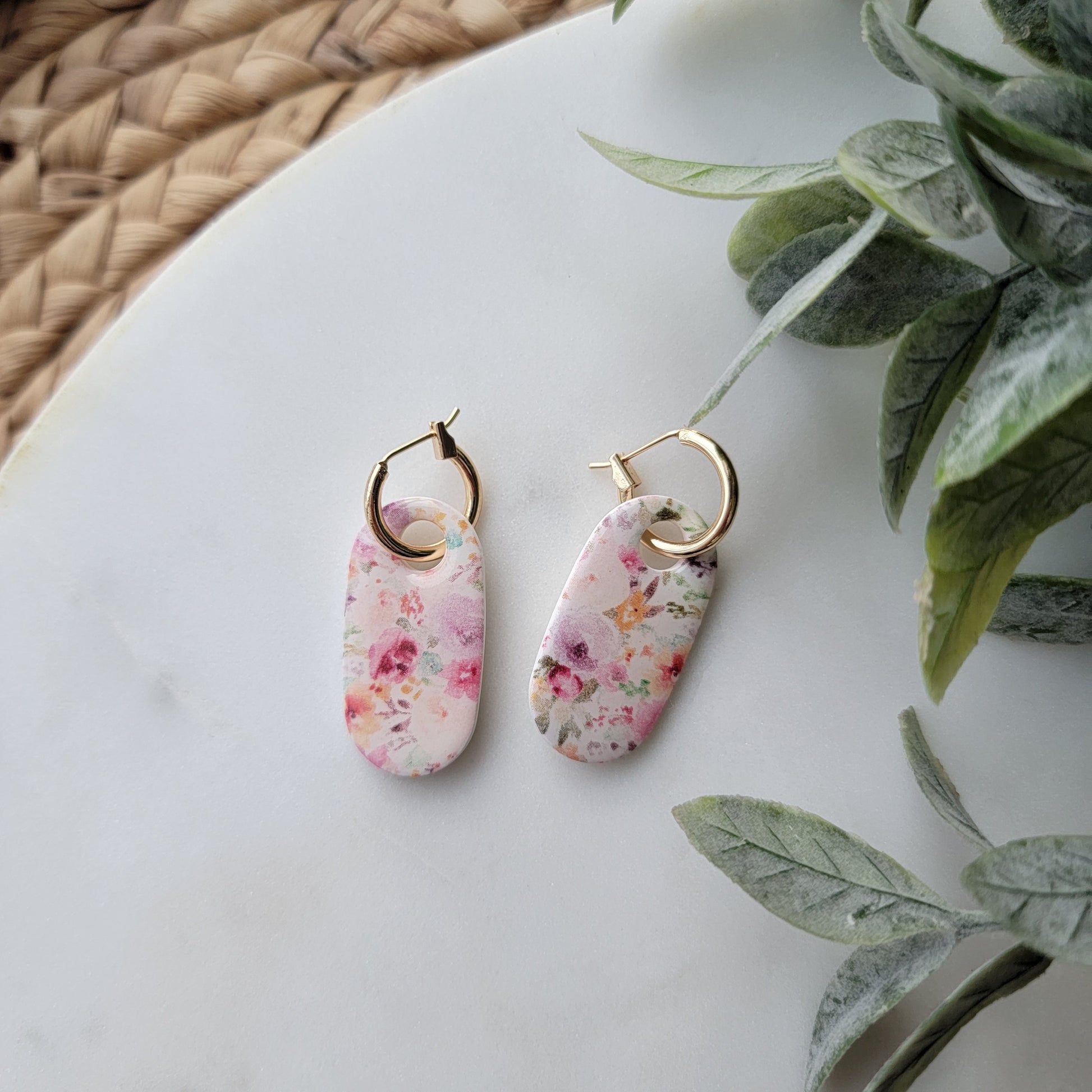 Floral earrings on a white surface with green leaves in the background