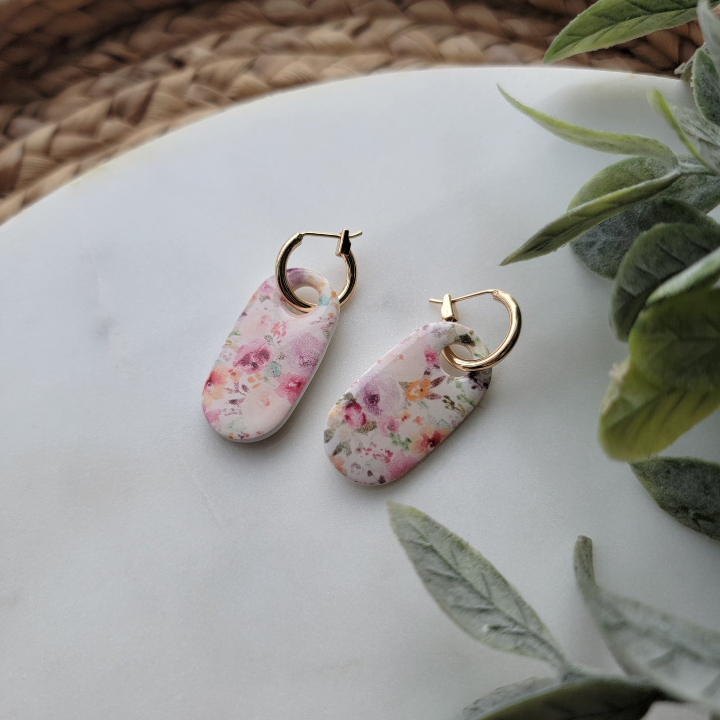 Floral earrings with gold hooks on a white surface with green leaves in the background