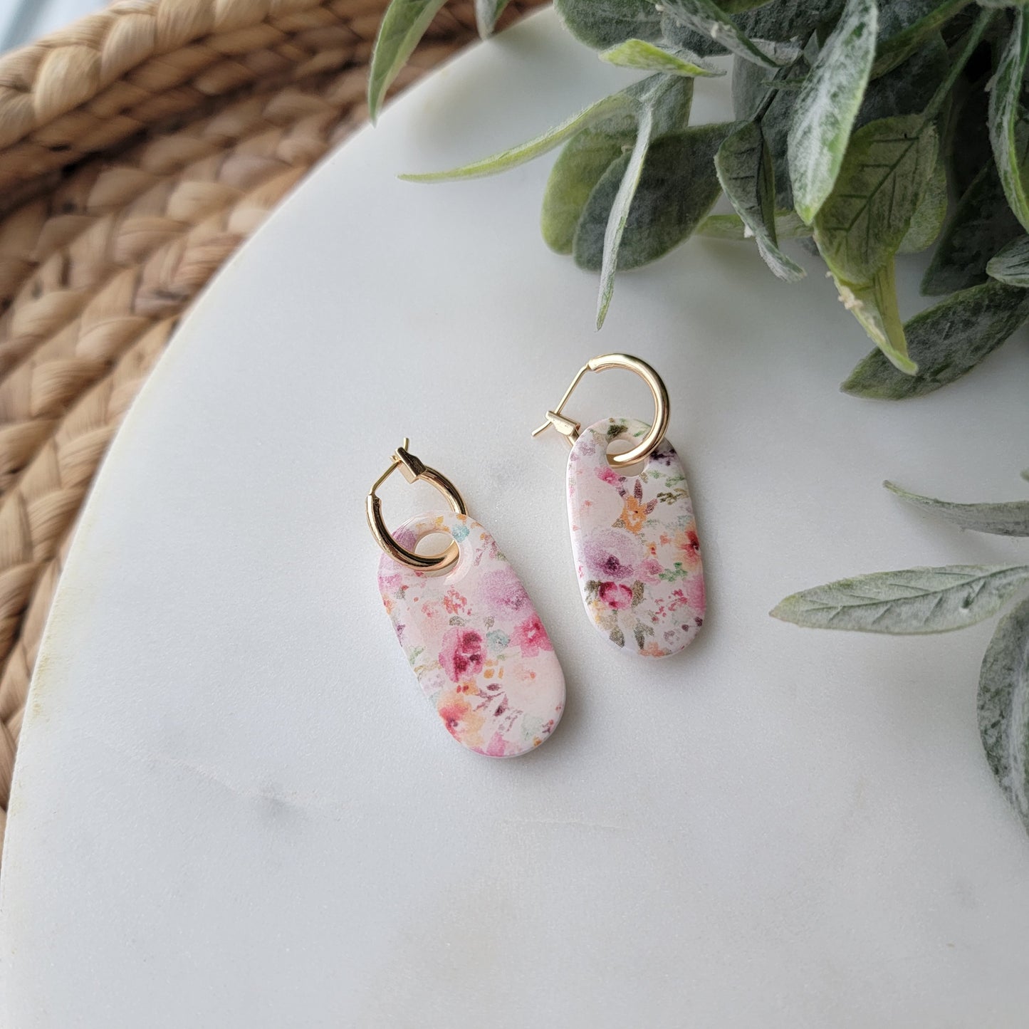 Floral charm earrings on a white surface with green leaves in the background