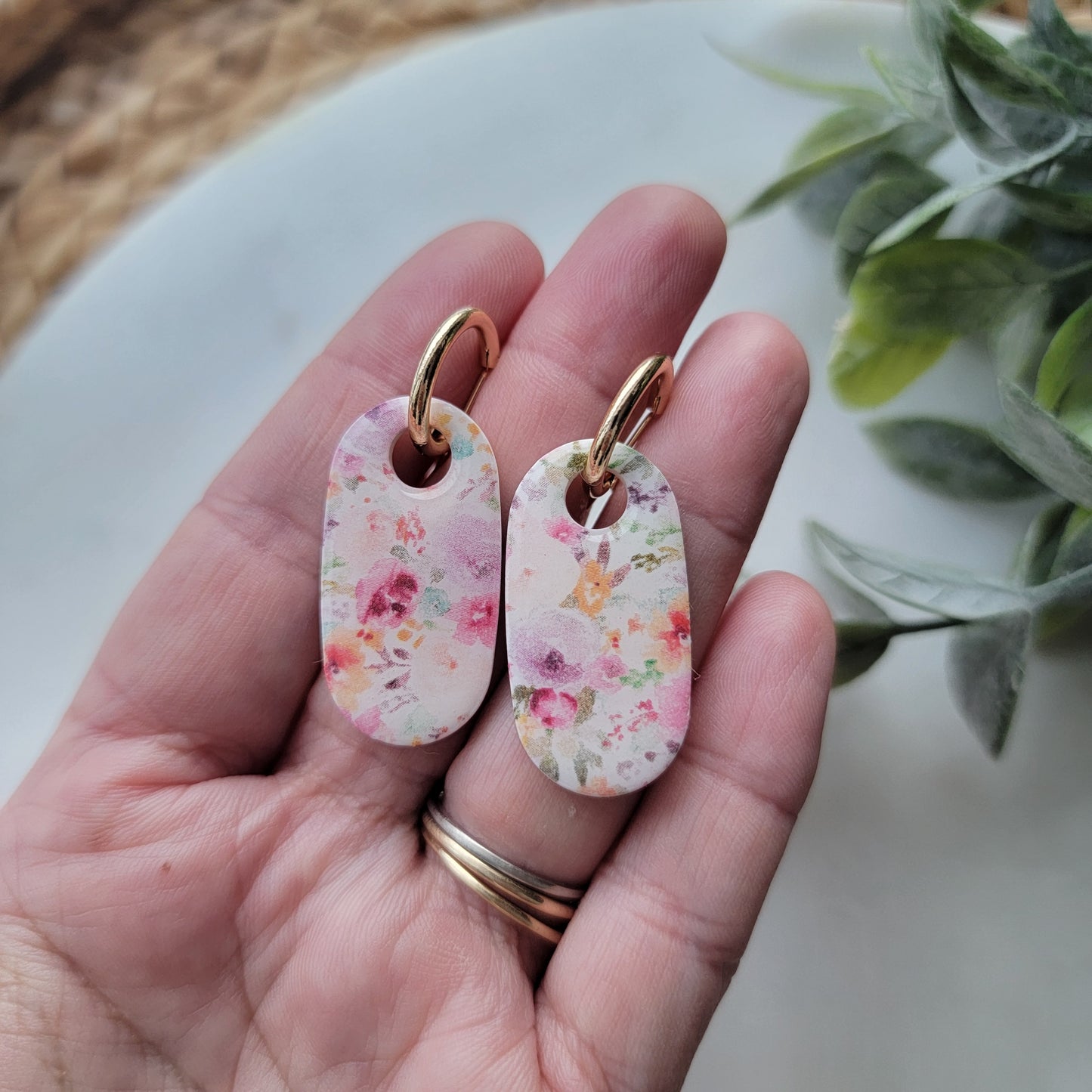 Hand holding floral earrings with a plant in the background