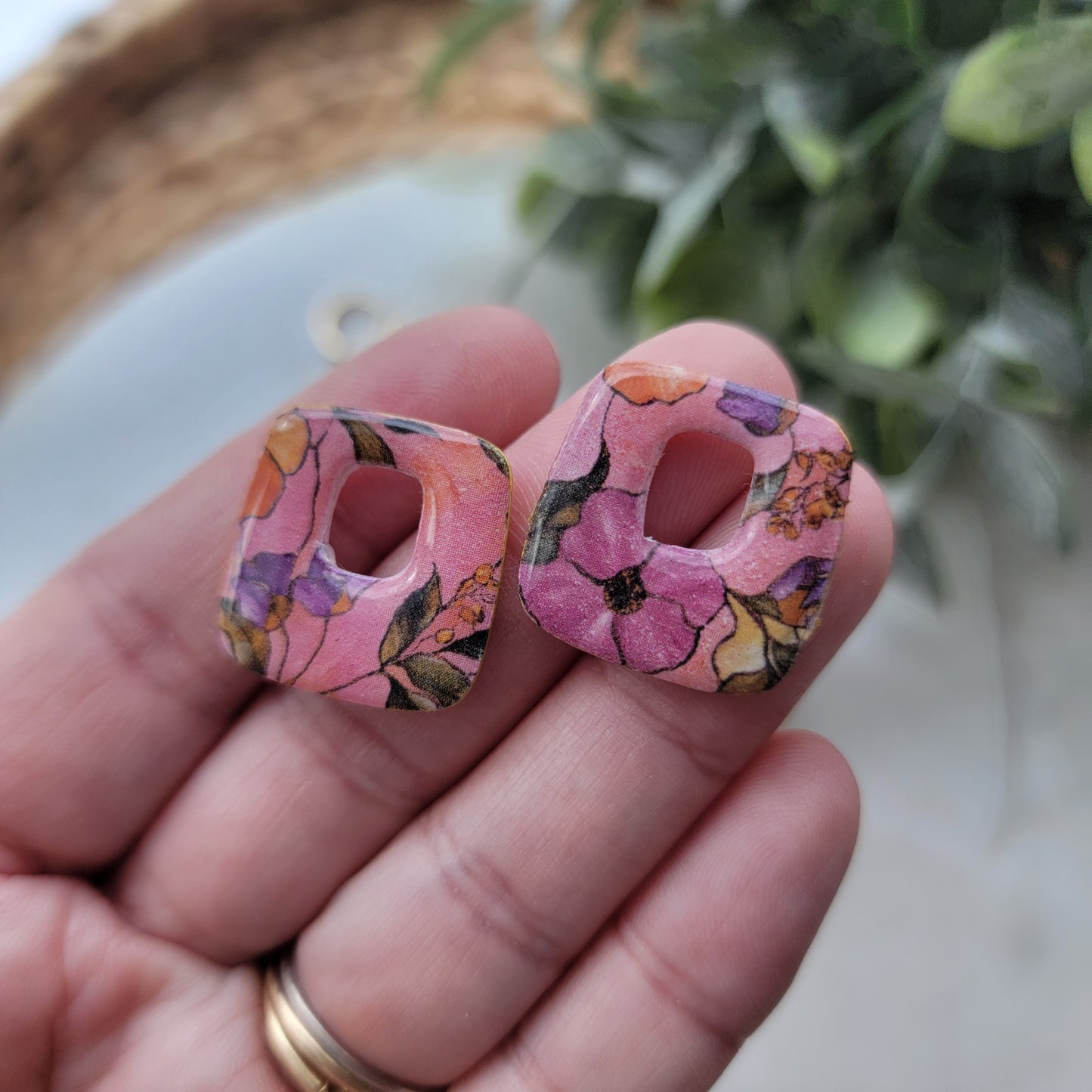 Hand holding a floral pink letter 'B' with a plant in the background