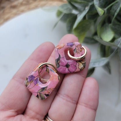 Floral patterned earrings held in a hand with a plant in the background