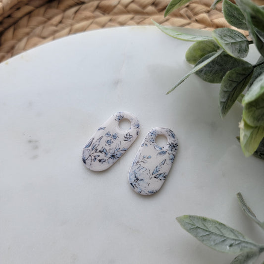 Floral-patterned ceramic tags on a marble surface with green leaves in the background