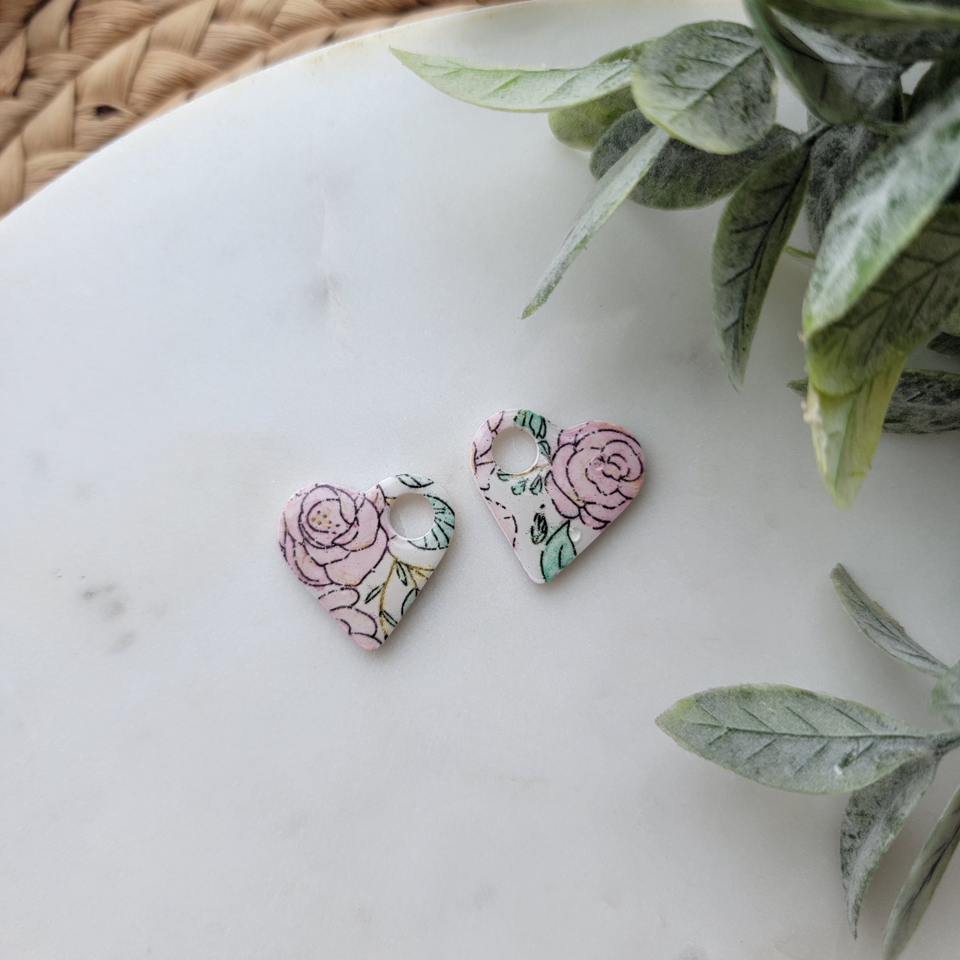 Heart-shaped earrings with floral design on a marble surface with leaves.