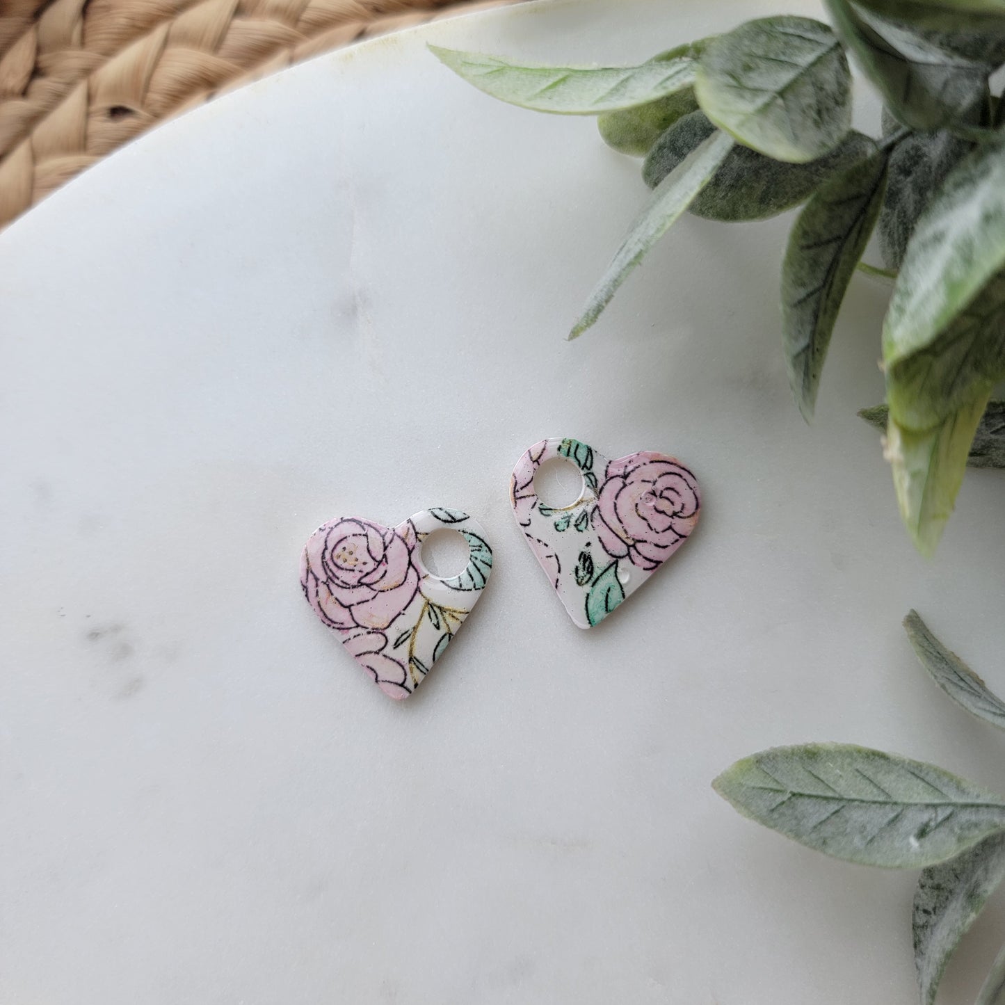 Floral earrings on a white surface with green leaves in the background