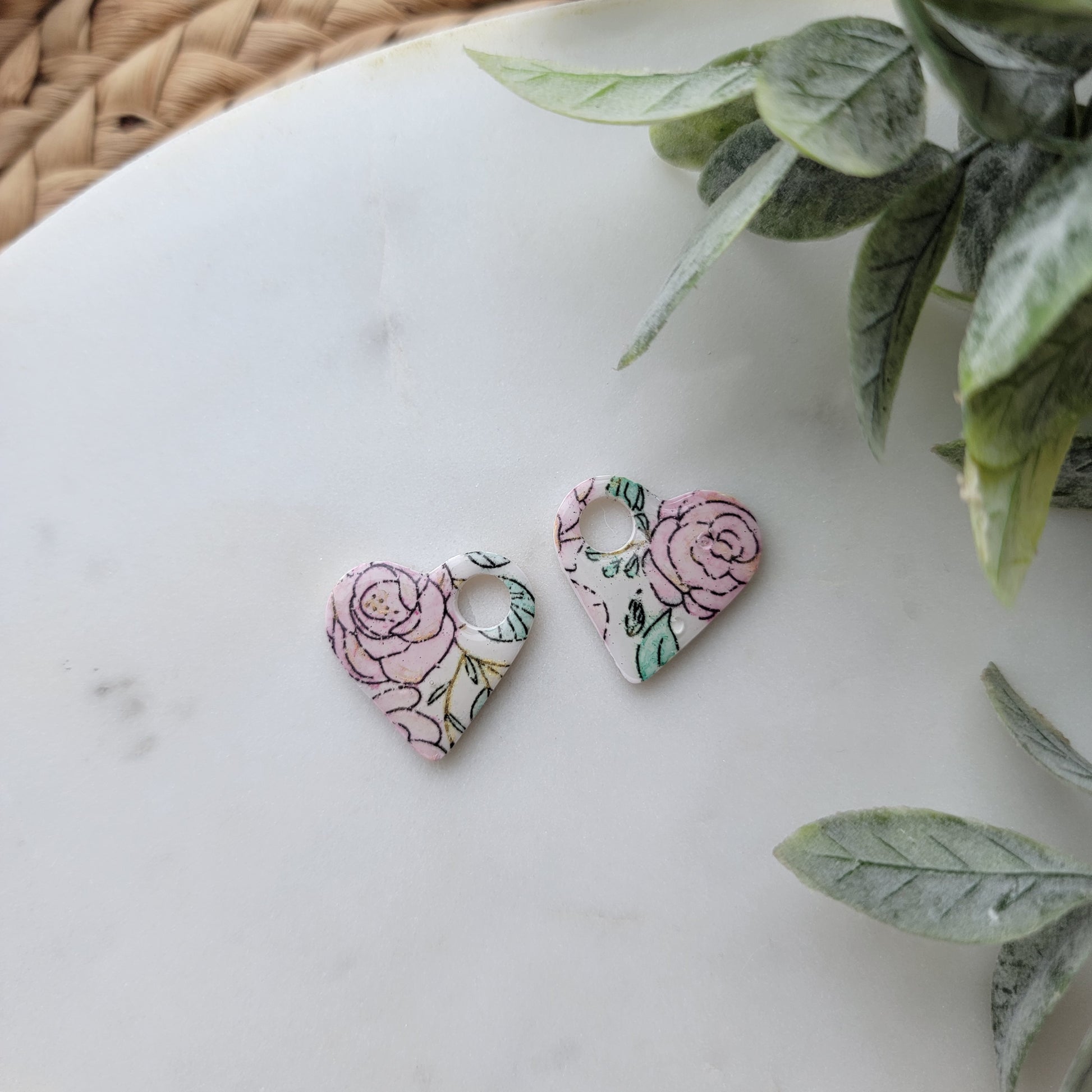 Floral earrings on a white surface with green leaves in the background