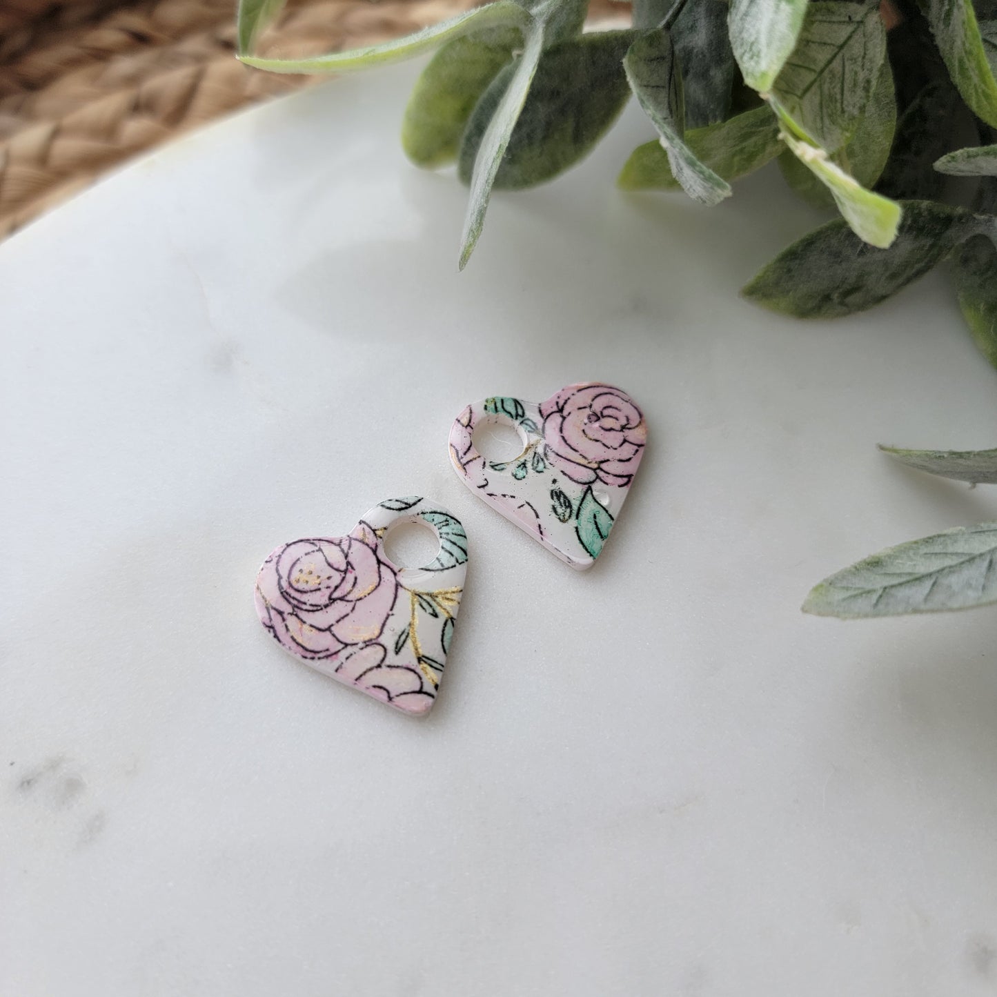 Floral-patterned earrings on a marble surface with green leaves in the corner.