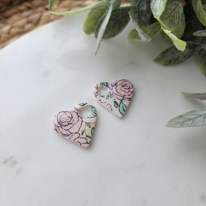 Floral-patterned earrings on a marble surface with green leaves in the corner.