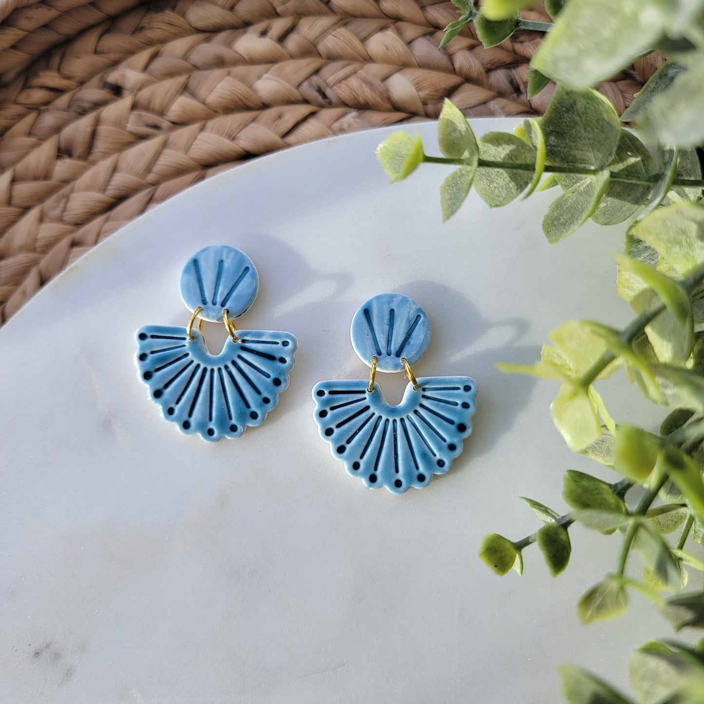 Blue earrings on a white surface with green leaves in the background