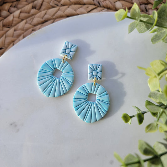 Pair of teal earrings on a marble surface with green leaves in the background