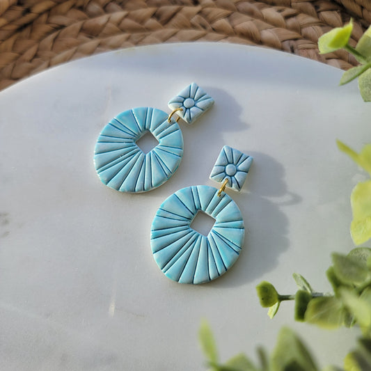 Pair of teal earrings on a marble surface with green leaves in the background