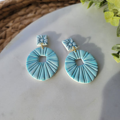 Pair of teal earrings on a marble surface with green leaves in the background