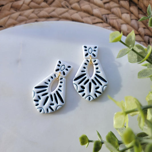 Pair of dark blue and white patterned earrings on a white surface with green leaves in the background