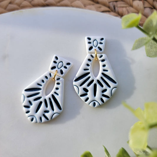 Pair of dark blue and white patterned earrings on a white surface with green leaves in the background