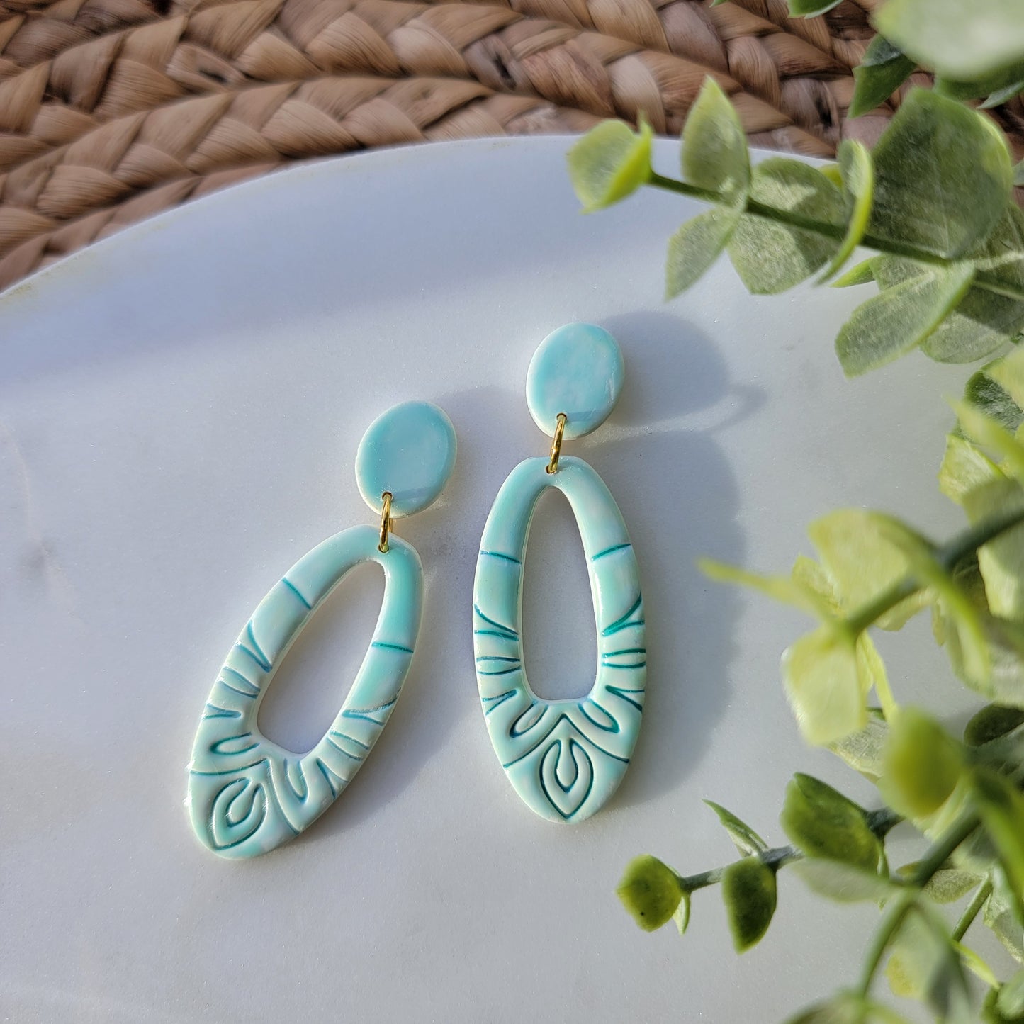 Turquoise ceramic earrings on a white plate with green leaves in the background