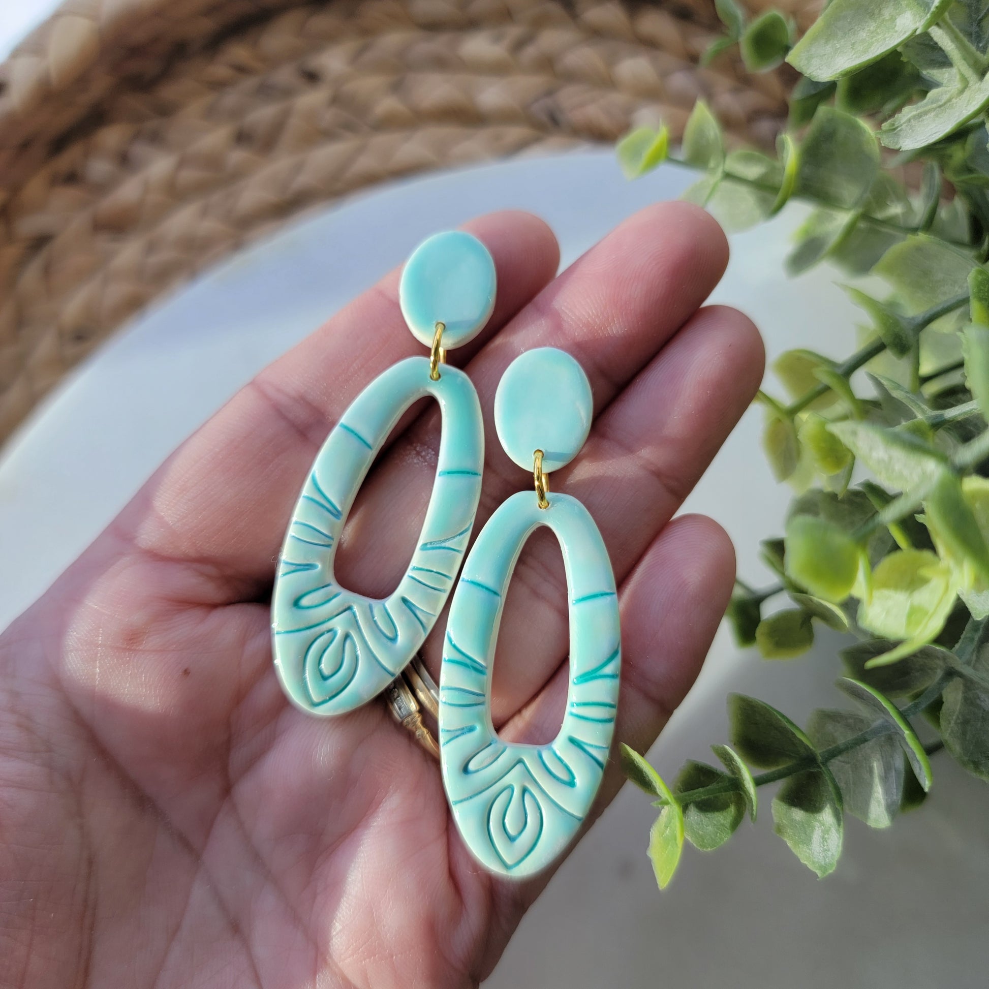 Turquoise earrings held in a hand with a blurred green plant background