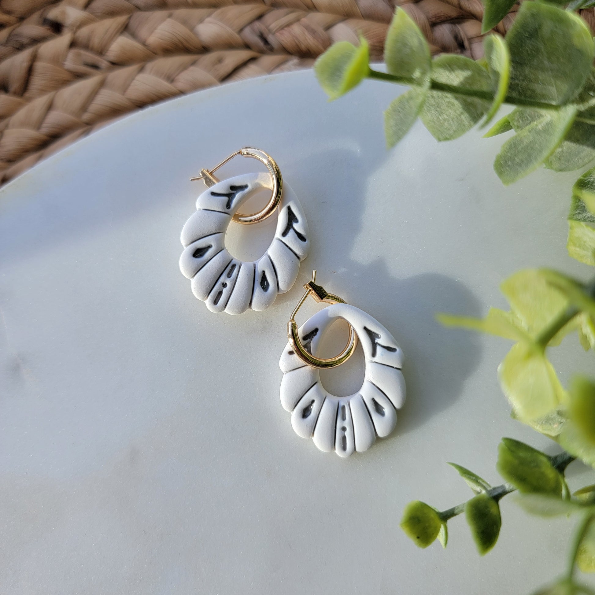 White earrings with gray accents in a ceramic style, adorned by a hoop earring.