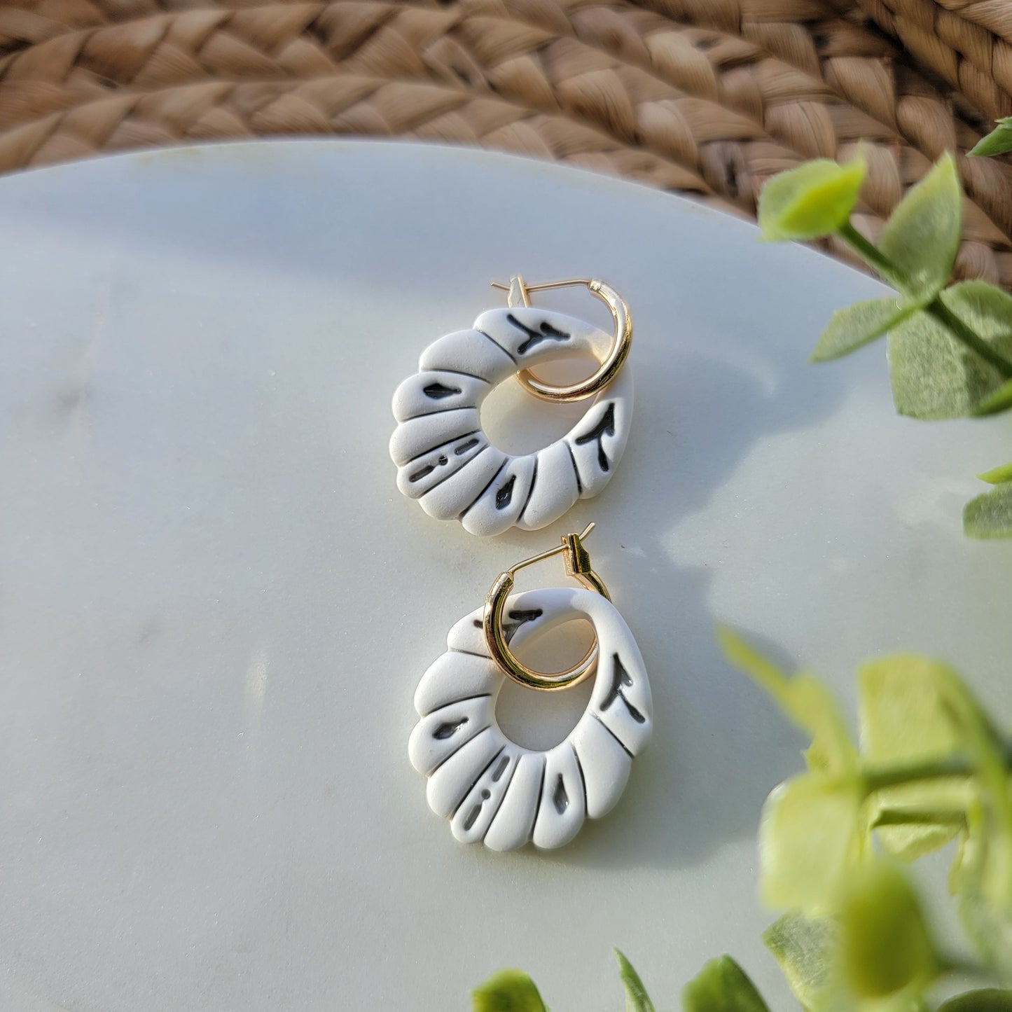 White earrings with gray accents in a ceramic style, adorned by a hoop earring.