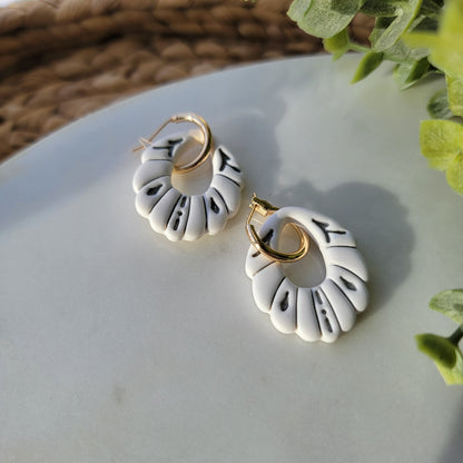White earrings with gray accents in a ceramic style, adorned by a hoop earring.