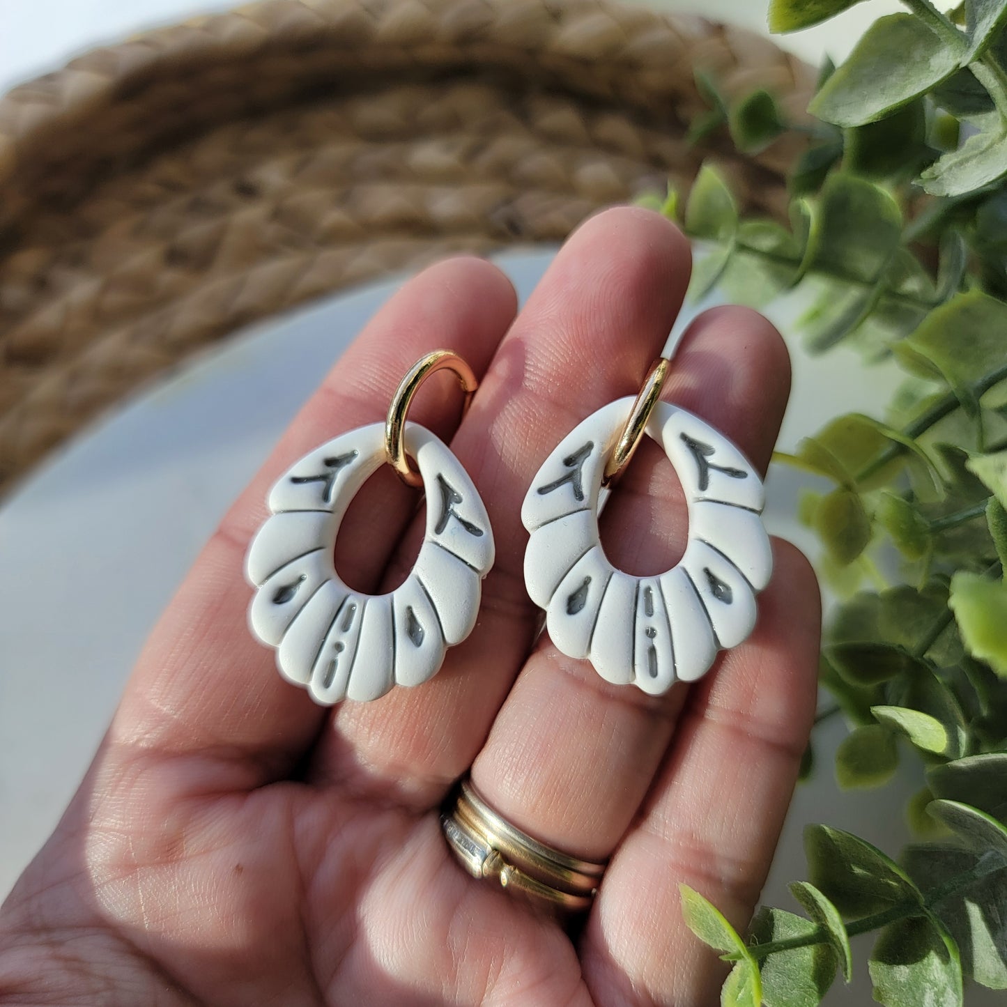 White earrings with gray accents in a ceramic style, adorned by a hoop earring, held in a hand.