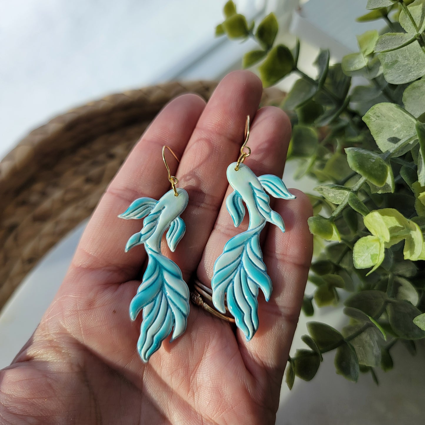 Koi fish earrings in a mix of blues and greens, held in a hand.