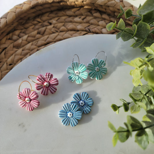 Floral earrings on a white surface with green leaves in the background