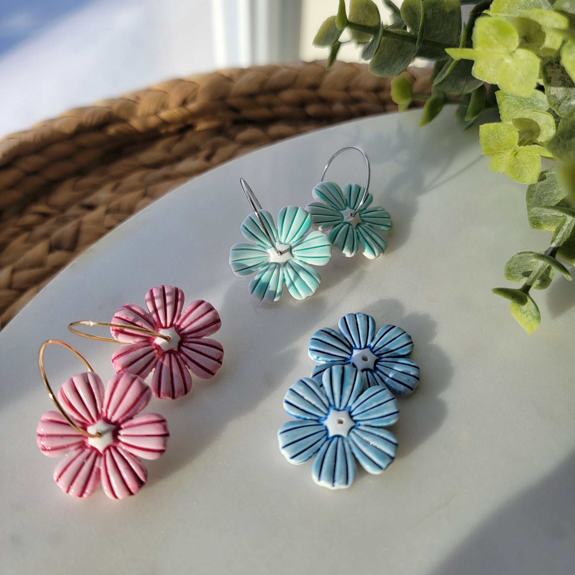 Pair of floral earrings on a light surface with greenery in the background