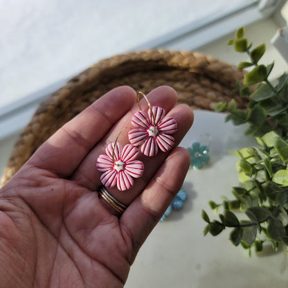 Hand holding pink flower-shaped earrings with a blurred background