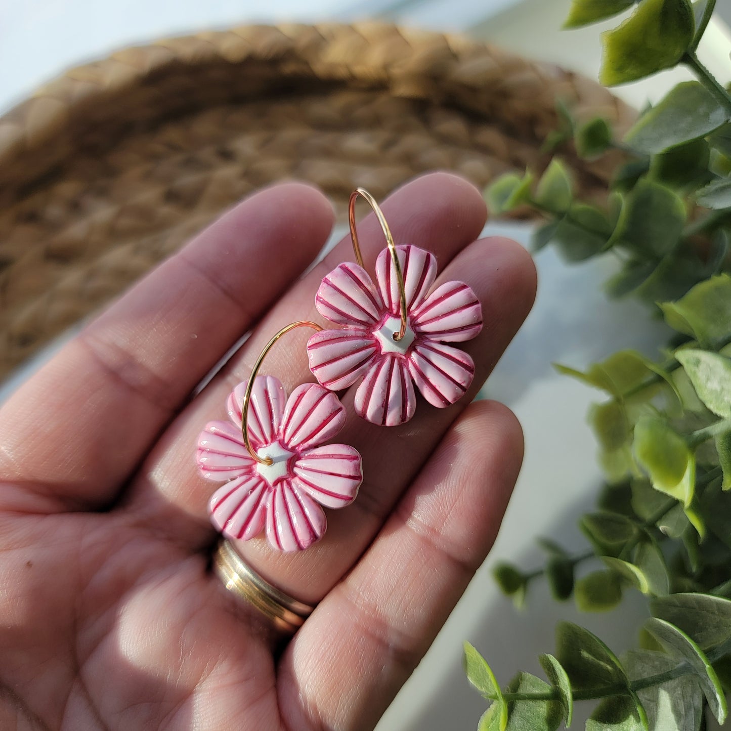Hand holding pink flower-shaped earrings with a blurred plant in the background