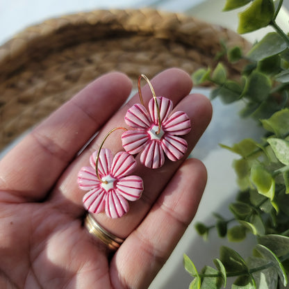 Hand holding pink flower-shaped earrings with a blurred plant in the background