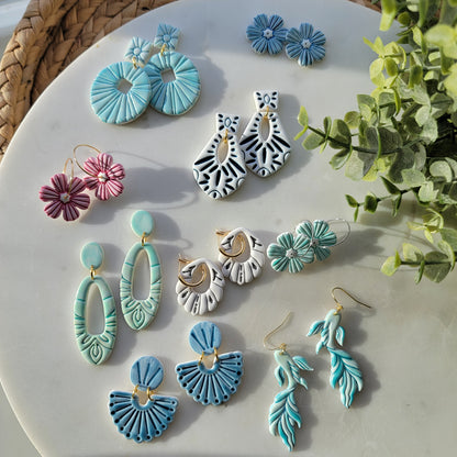 Assorted earrings on a white surface with greenery in the background