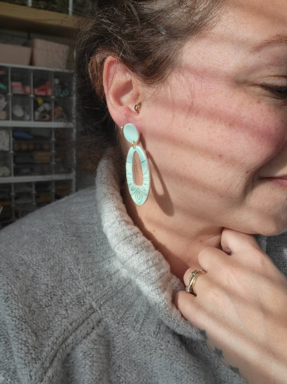 Person wearing a gray sweater with a seafoam colored earring, showing sizing of earrings.