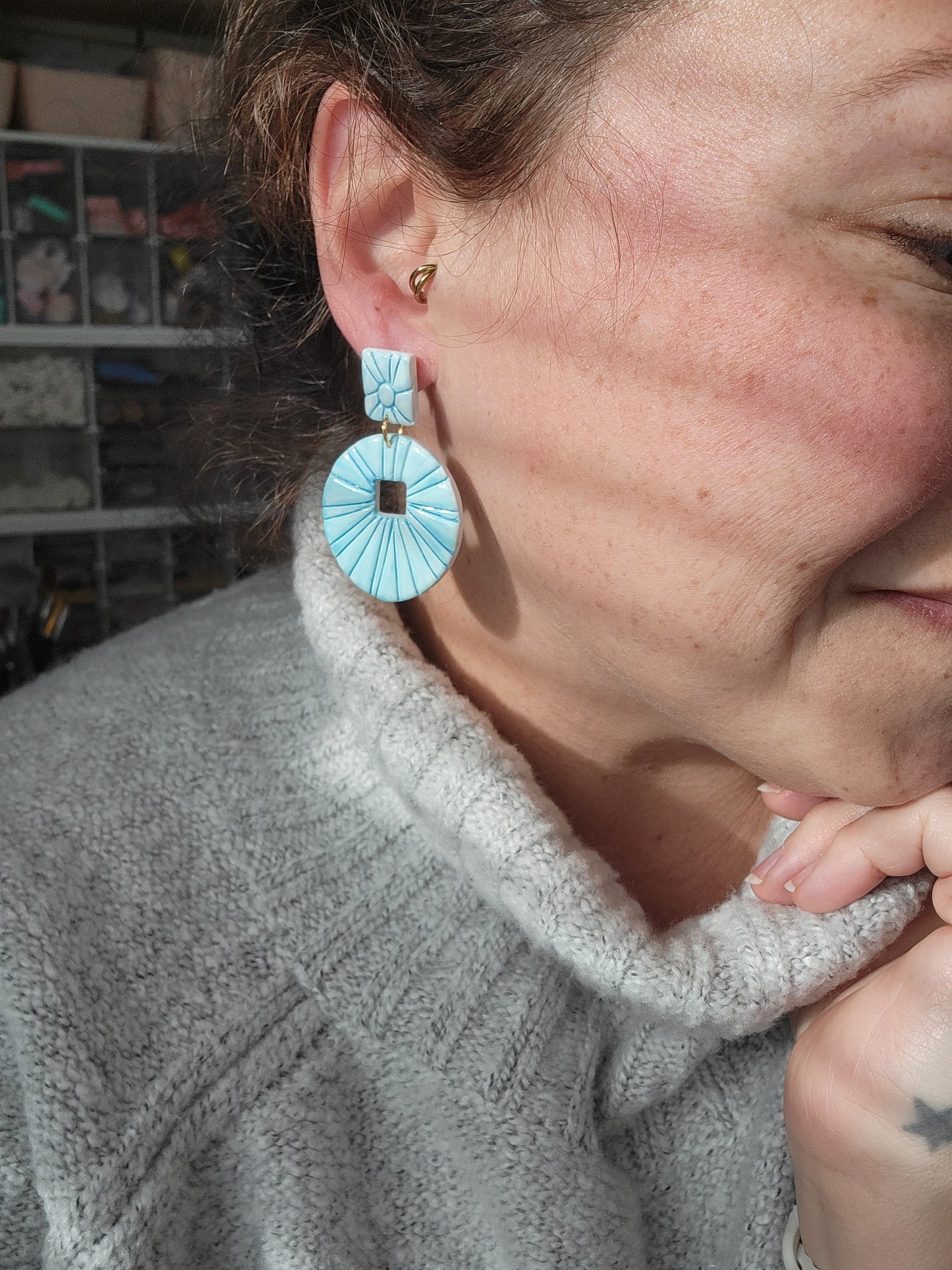 Person wearing a gray sweater with teal earrings, showing sizing of earrings.