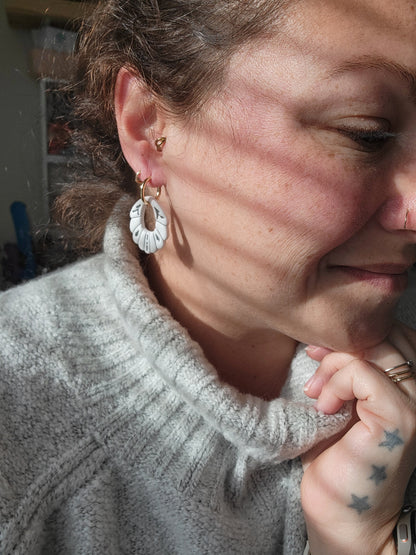 Person wearing a gray sweater with white and gray earrings, showing sizing of earrings.