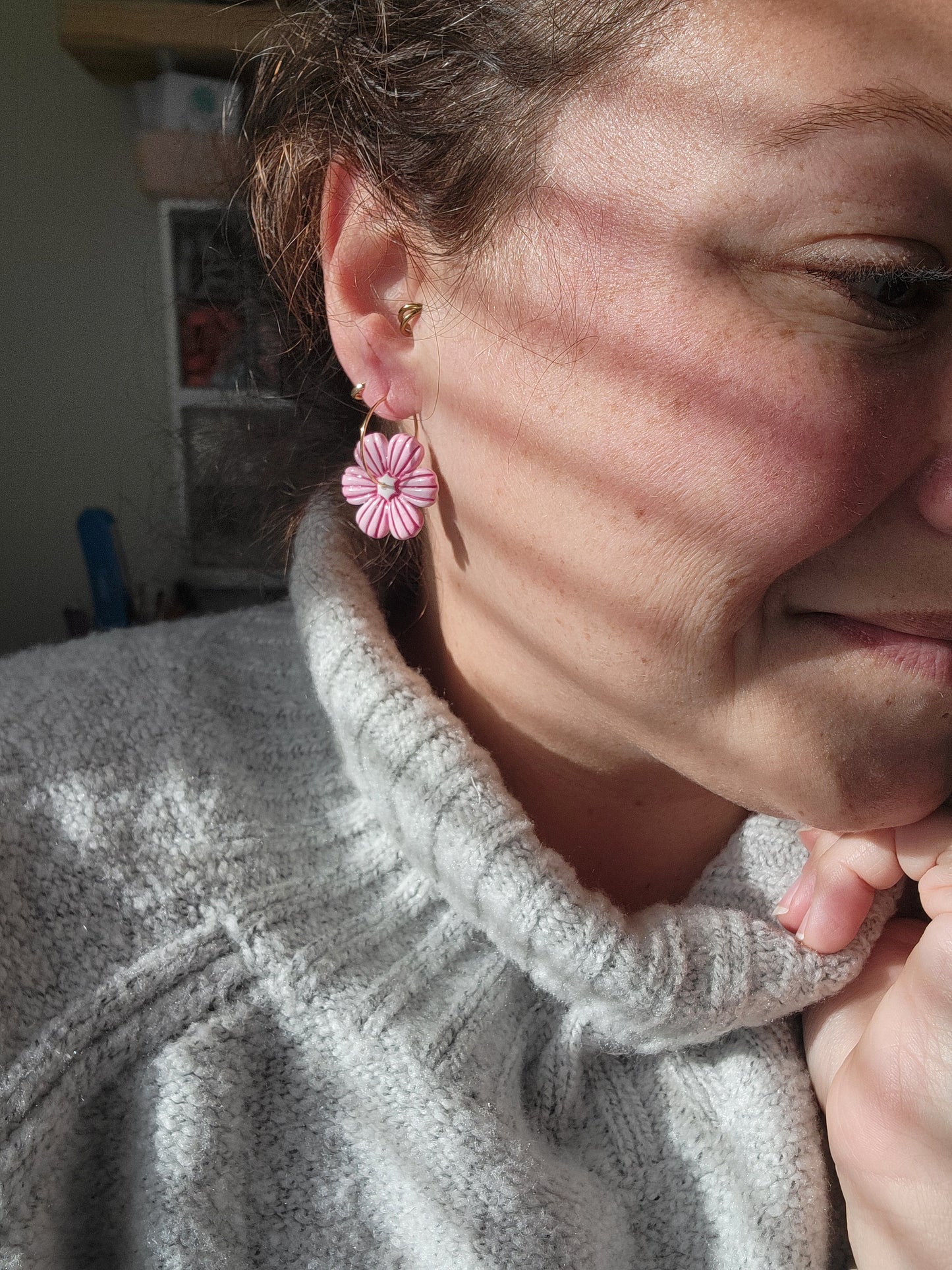 Person wearing a gray sweater with a pink flower hoop earring, showing sizing of earrings.