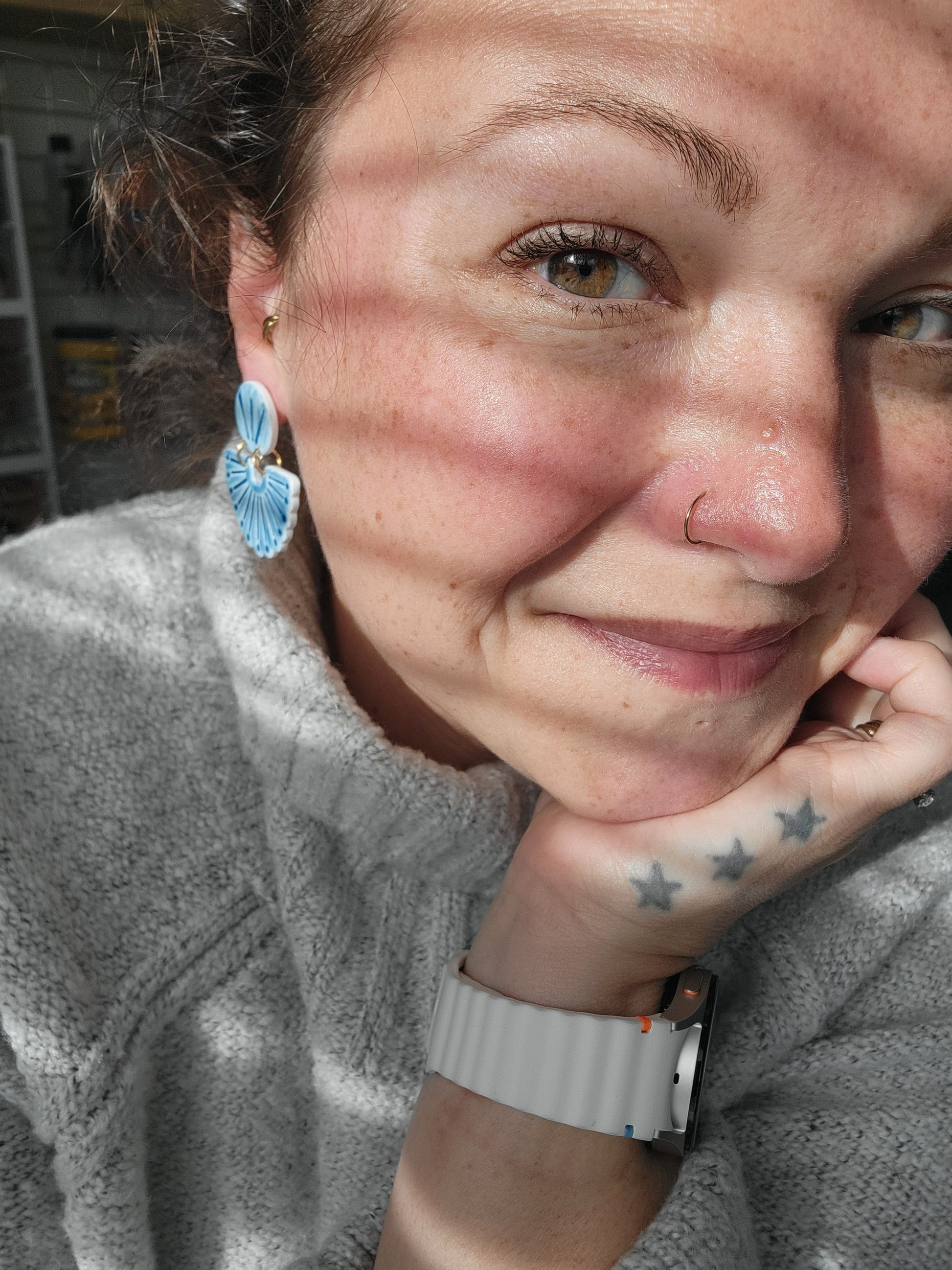 Person wearing a gray sweater with a blue scalloped earrings, showing sizing of earrings.