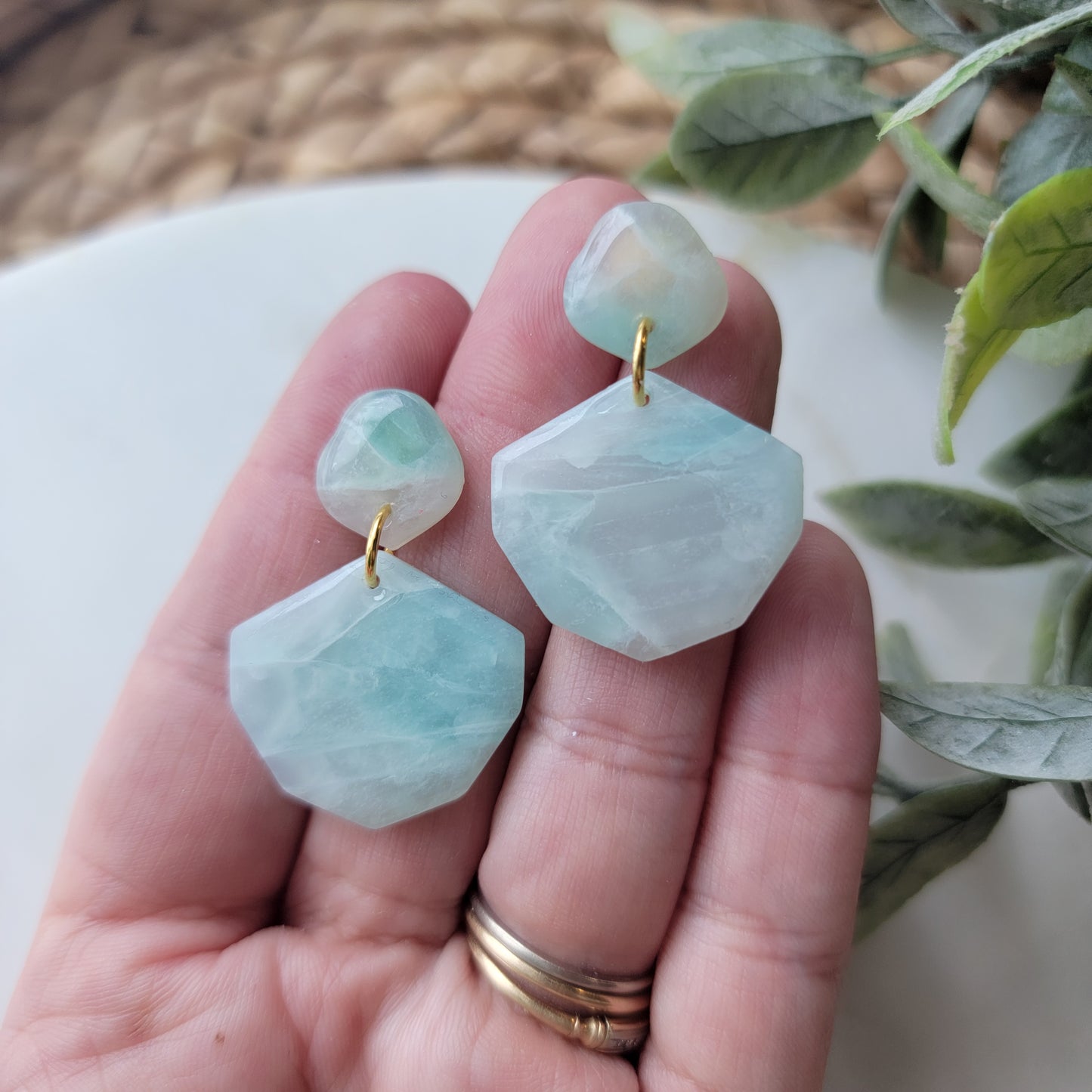 Hand holding light blue stone designed earrings. 