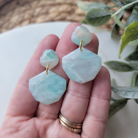 Hand holding light blue stone designed earrings. 