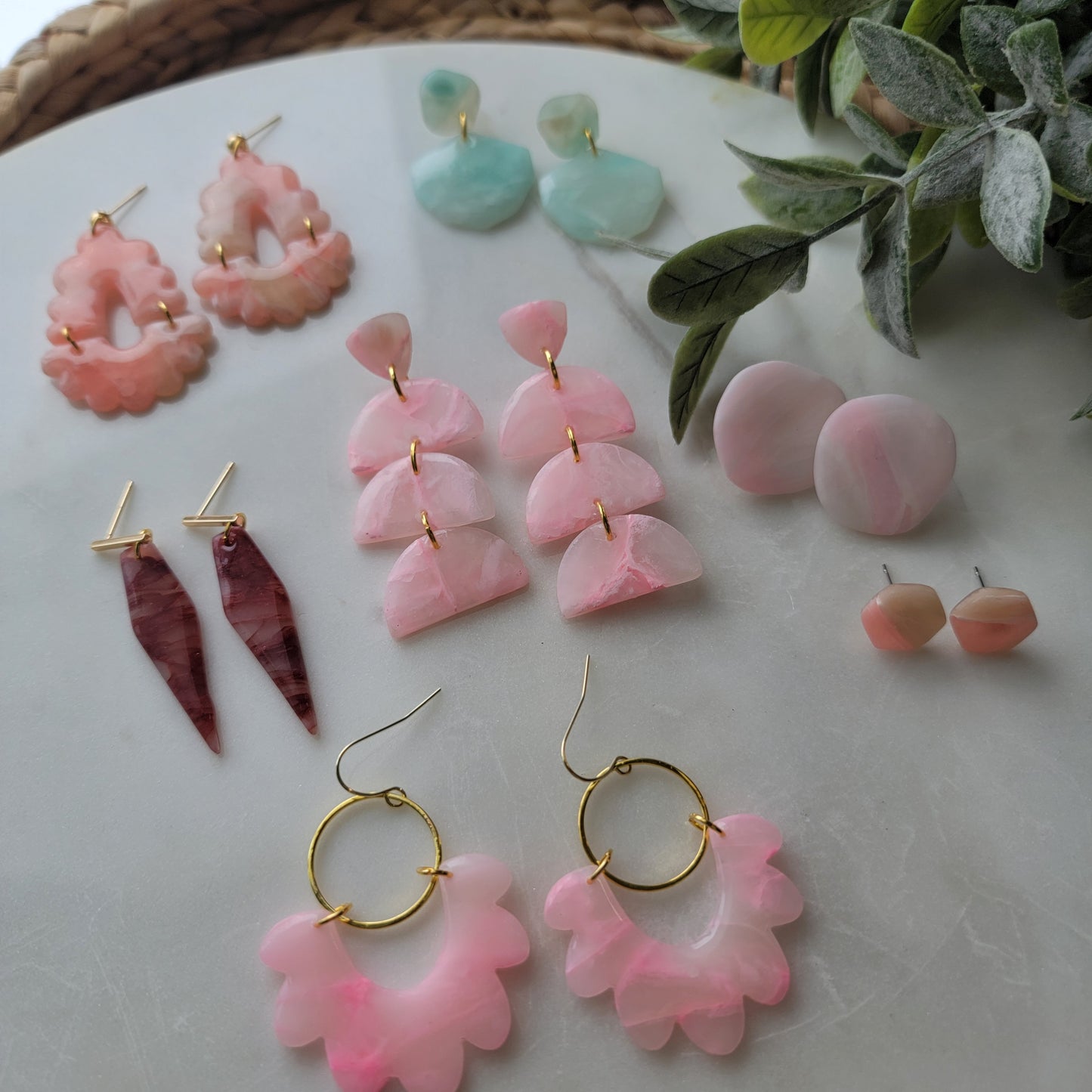 Collection of pink and gold earrings on a marble surface with green leaves.