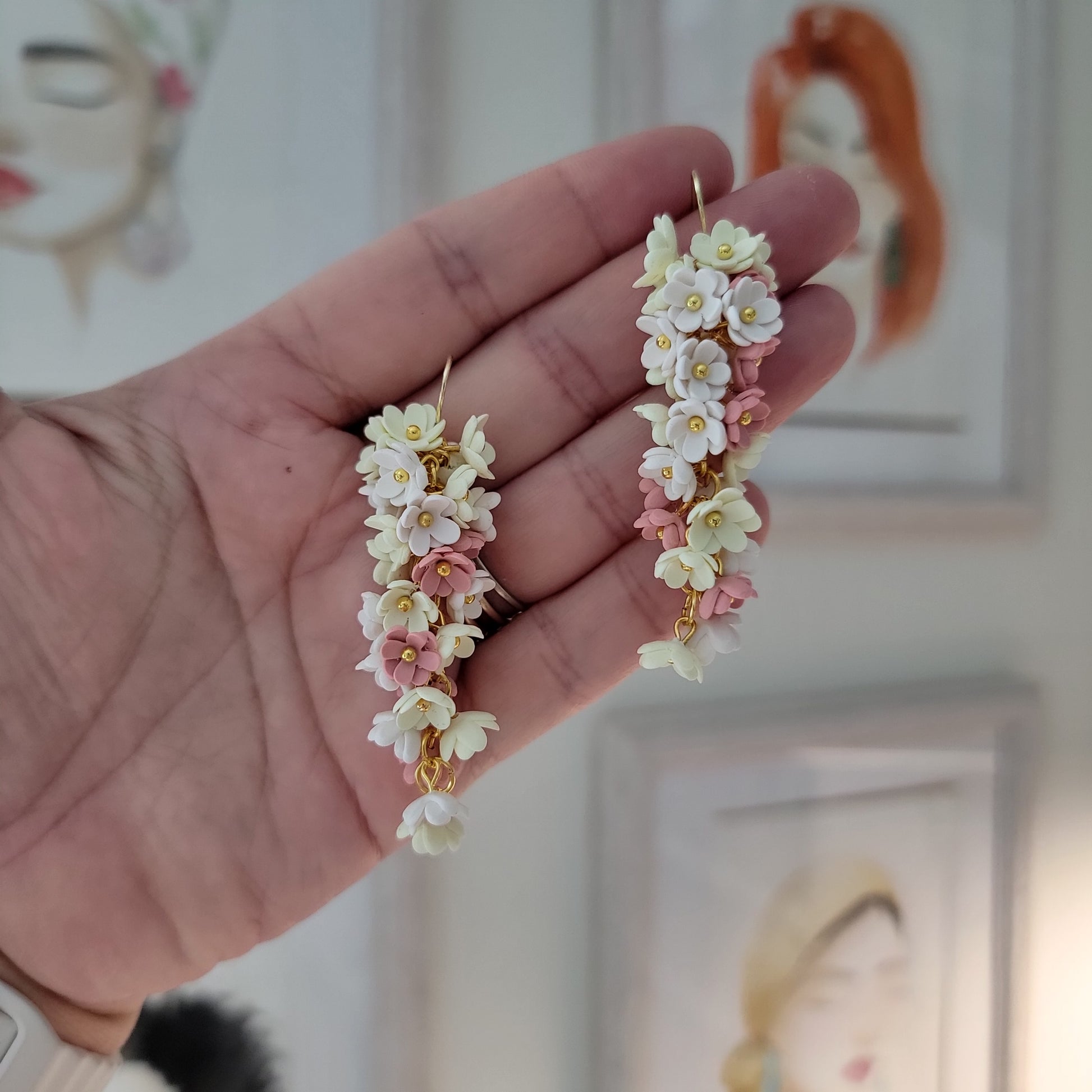 Pink, yellow and white flowers decorated earrings held by a hand.
