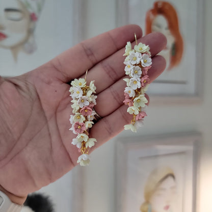 Pink, yellow and white flowers decorated earrings held by a hand.
