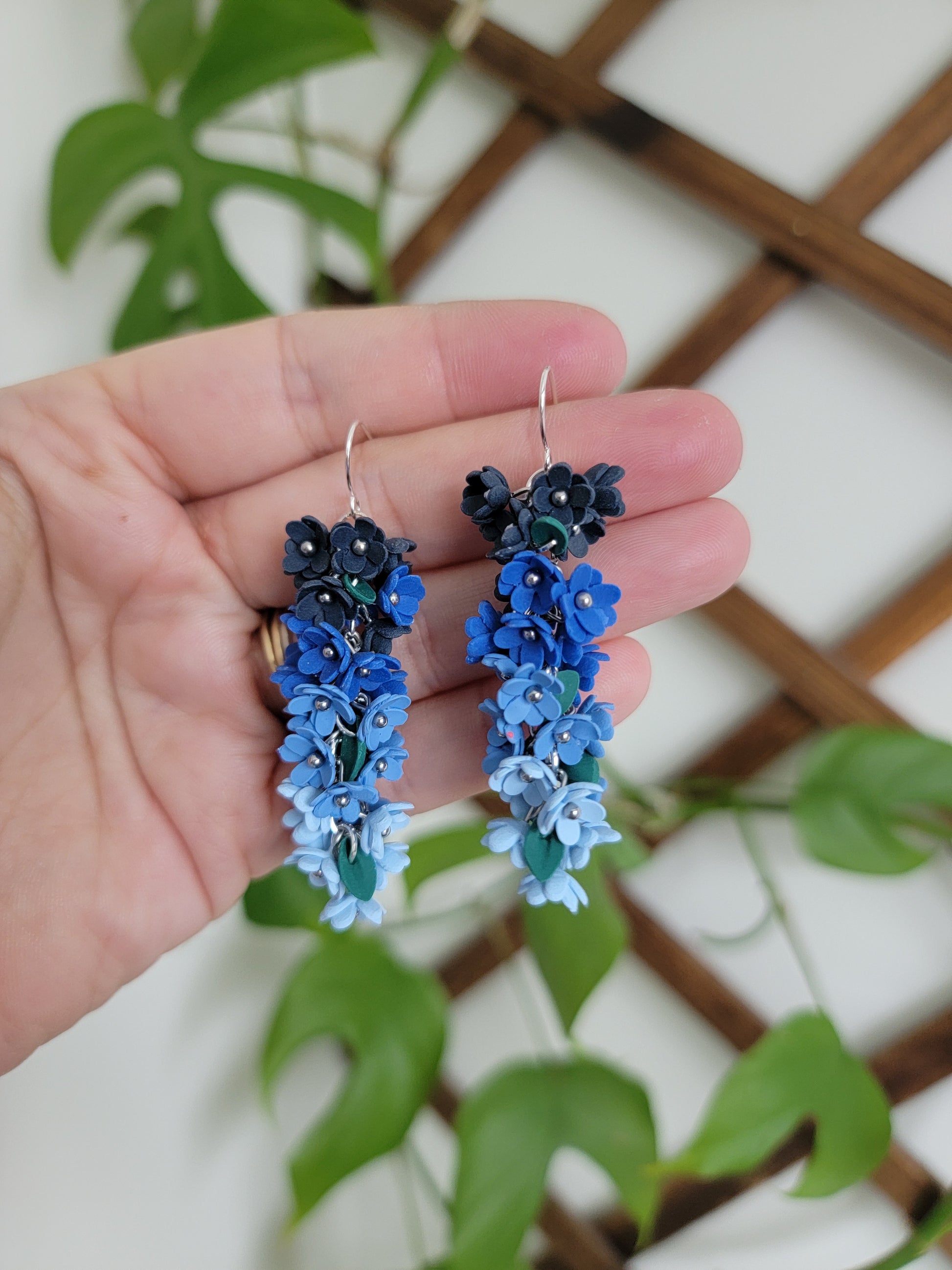 Blue floral earrings held in a hand with a green leafy background
