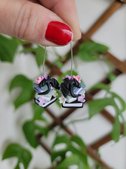 A set of earrings featuring colorful book stacks with dainty flowers and a black dragon on them.