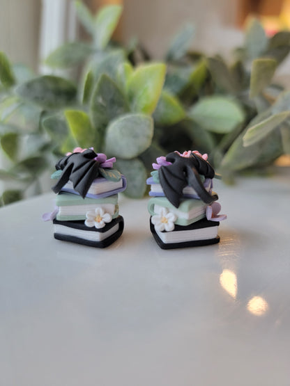 A set of earrings featuring colorful book stacks with dainty flowers and a black dragon on them.