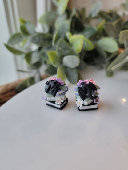 A set of earrings featuring colorful book stacks with dainty flowers and a black dragon on them.