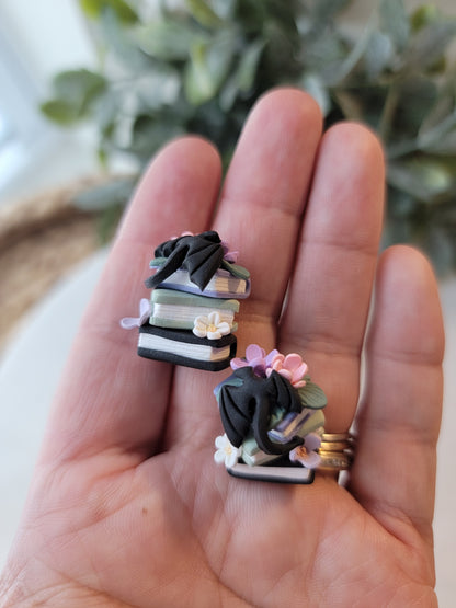 A set of earrings featuring colorful book stacks with dainty flowers and a black dragon on them.