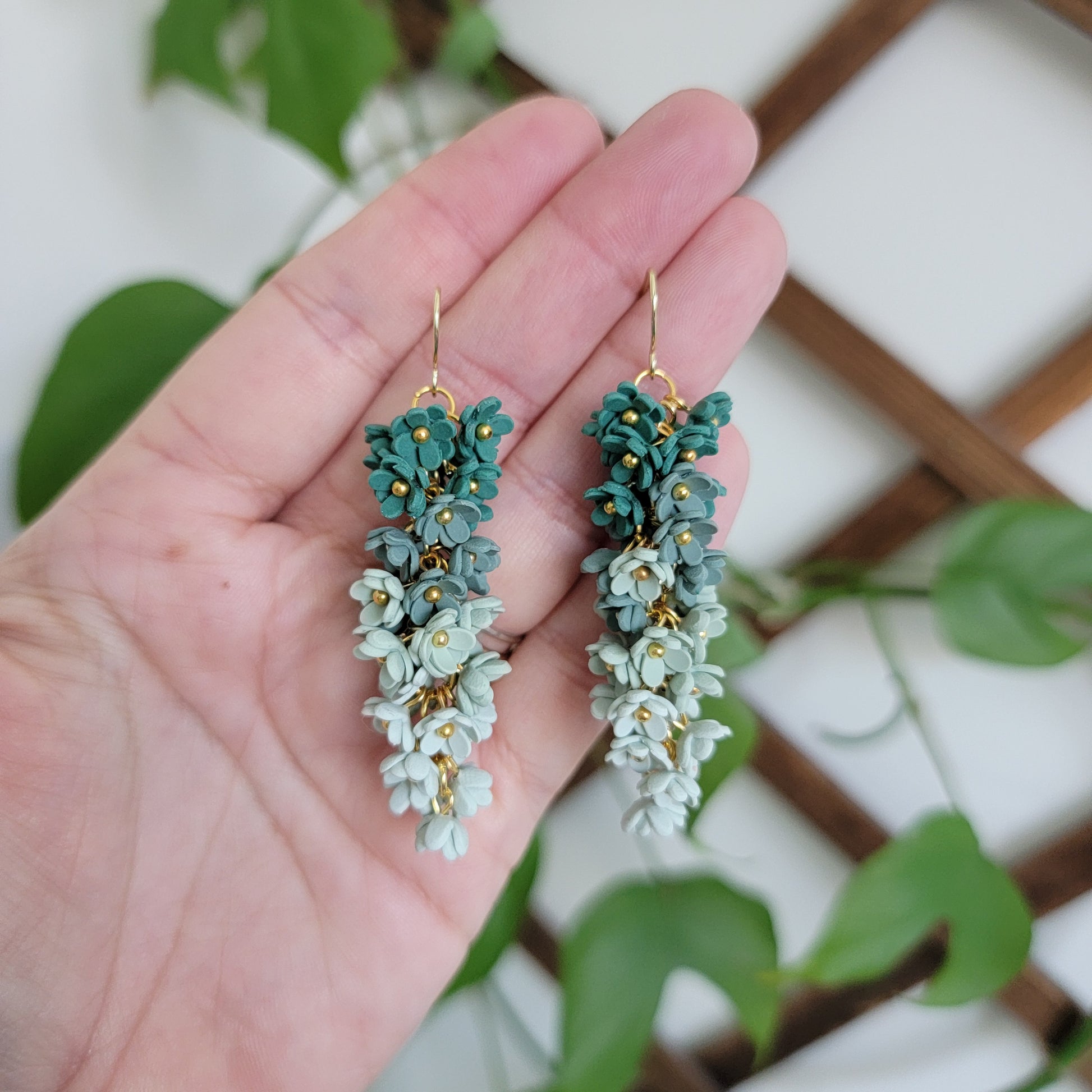 Green floral earrings held by a hand.